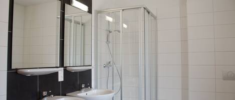 A bathroom with two sinks, a glass shower enclosure, and a large mirror with under-cabinet lighting.