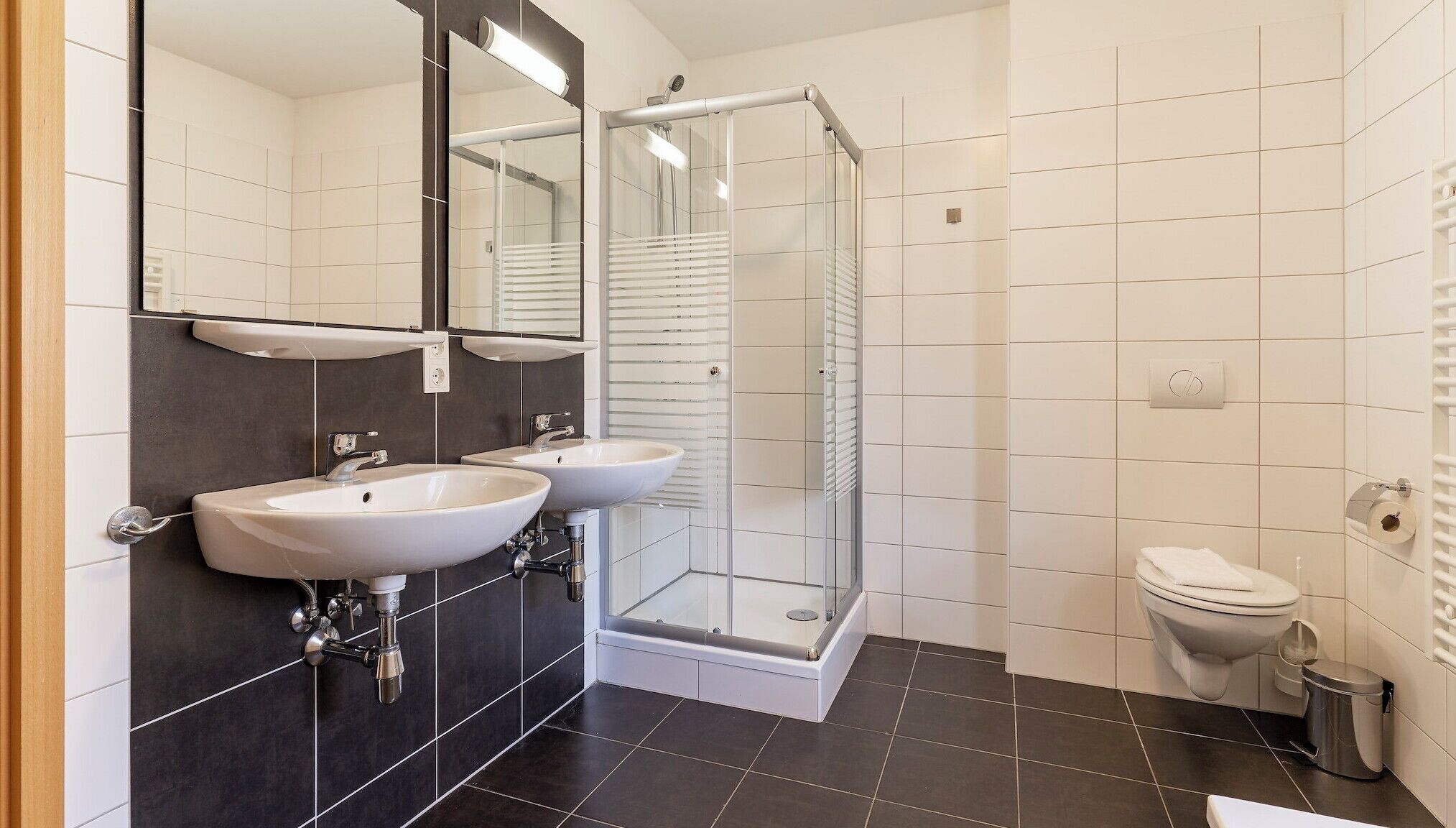 A modern bathroom with two sinks, a glass shower enclosure, and a toilet.