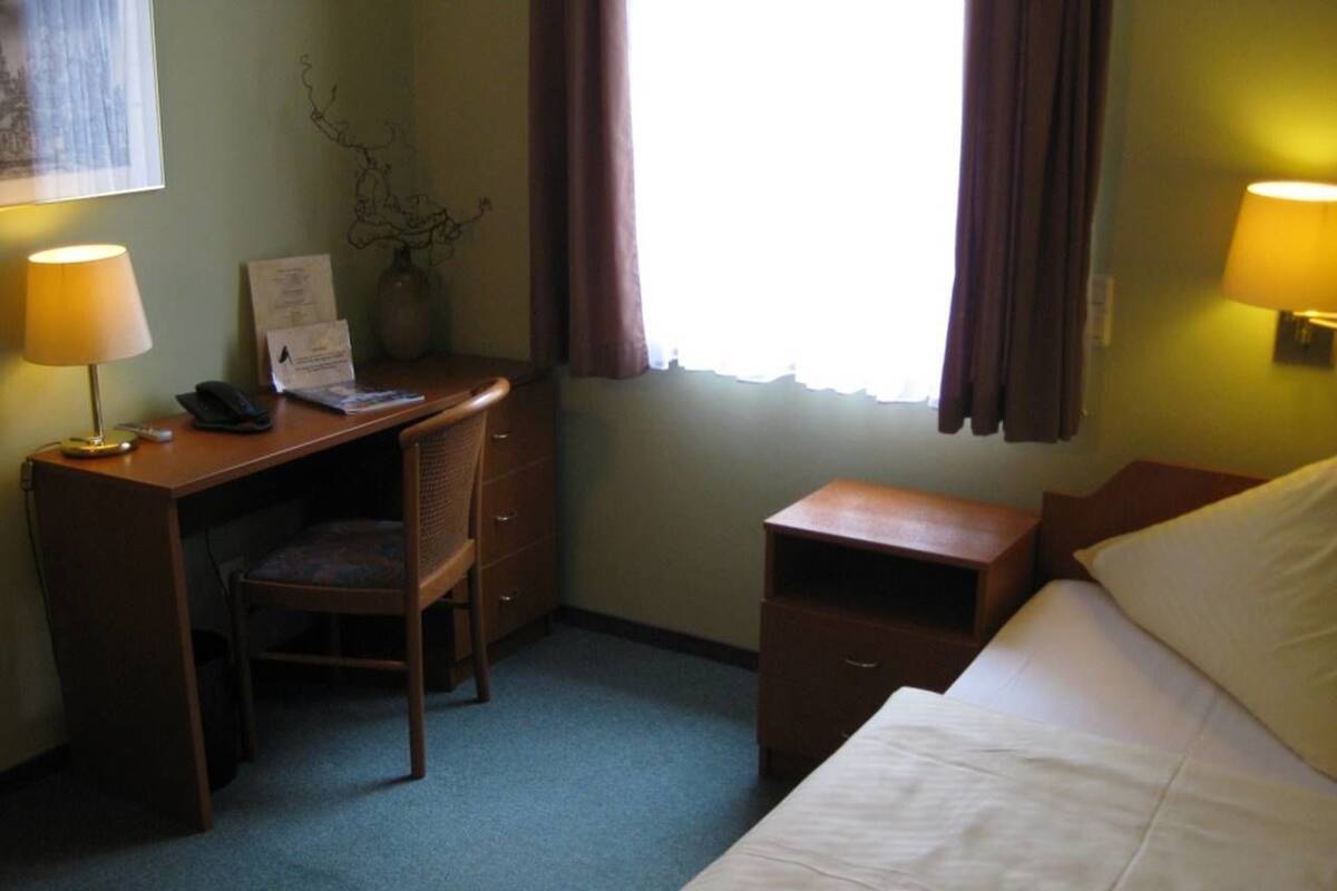 Une chambre d’hôtel avec un lit, un bureau, une chaise et une petite table de chevet.