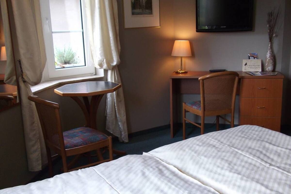 Une chambre d’hôtel équipée d’un lit, d’un bureau, d’une chaise, d’une télévision et d’une fenêtre avec des rideaux.