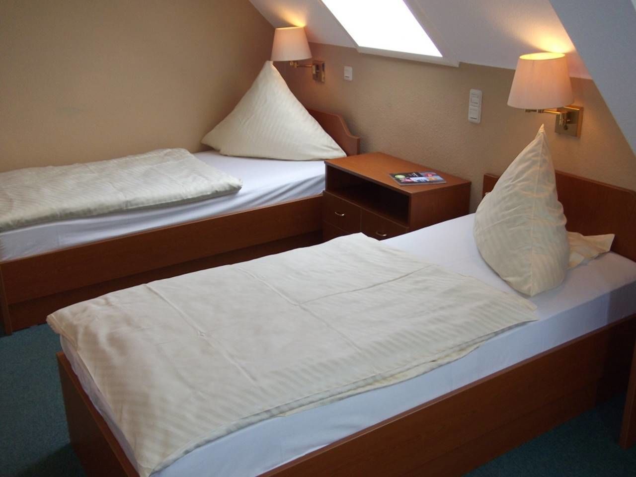 Una habitación pequeña y acogedora con dos camas individuales, una mesita de noche y una lámpara.