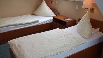 Una habitación pequeña y acogedora con dos camas individuales, una mesita de noche y una lámpara.