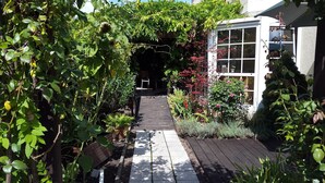 Een tuinpad dat leidt naar een gebouw met een glazen deur, omringd door weelderige begroeiing en verschillende planten.
