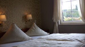 Een hotelkamer met een groot bed, twee bedlampen, een raam met gordijnen en behangpapier met een patroon.