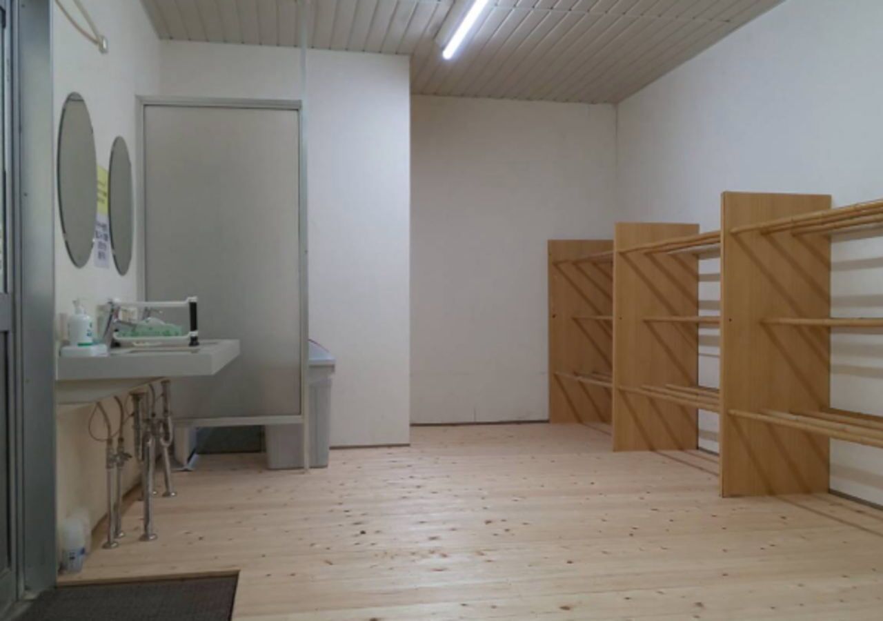 Een kamer met een houten vloer, een witte muur met een spiegel, een wastafel en een houten rek.