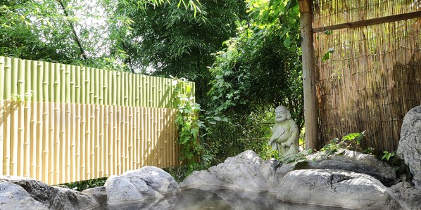 Un jardín tranquilo con valla de bambú, una estatua de piedra y una formación rocosa.