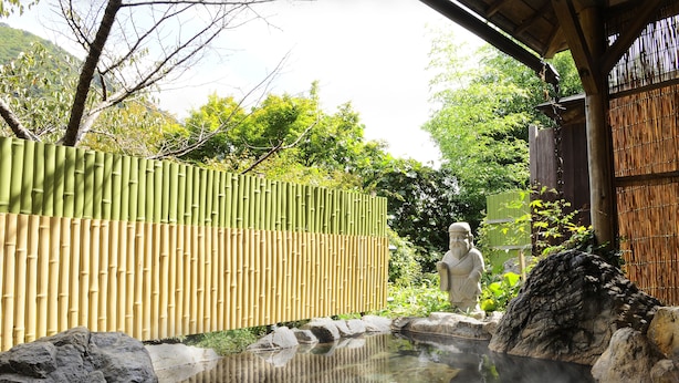 Ein traditioneller japanischer Garten mit einer Steinfigur, einem Bambuszaun und einer Thermalquelle.