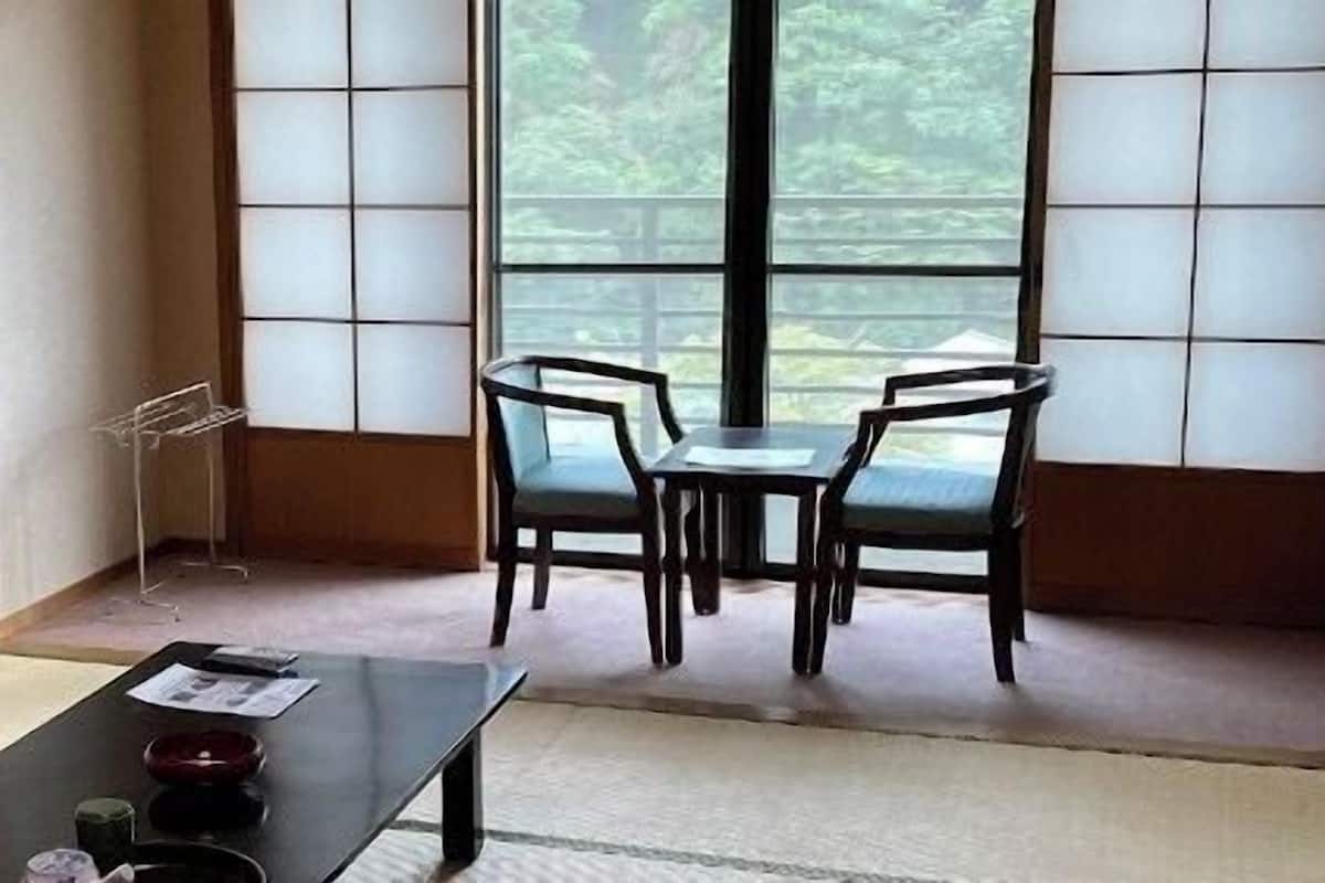 A traditional Japanese room with tatami flooring, a low table with a tea set, and a view through shoji screens.