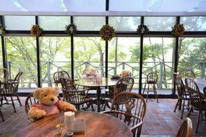 A dining area with round tables and chairs, a teddy bear on one table, and sunflowers on the windowsills.