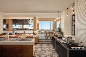 A modern kitchen with a buffet setup, a view of the city, and a large island with various food items.