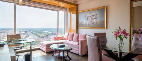 A spacious living room with a large window, a pink sofa, a glass coffee table, and a painting on the wall.