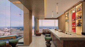 A modern bar area with a city view, seating, and a bar stocked with bottles. - Renaissance Lucknow Hotel (Lucknow)
