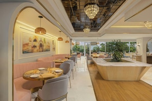 Un restaurante moderno con mesas redondas, asientos acolchados, candelabros y un cuadro grande en la pared.