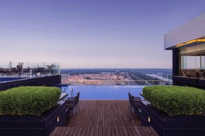 A rooftop pool with a city view, wooden deck, and seating areas.