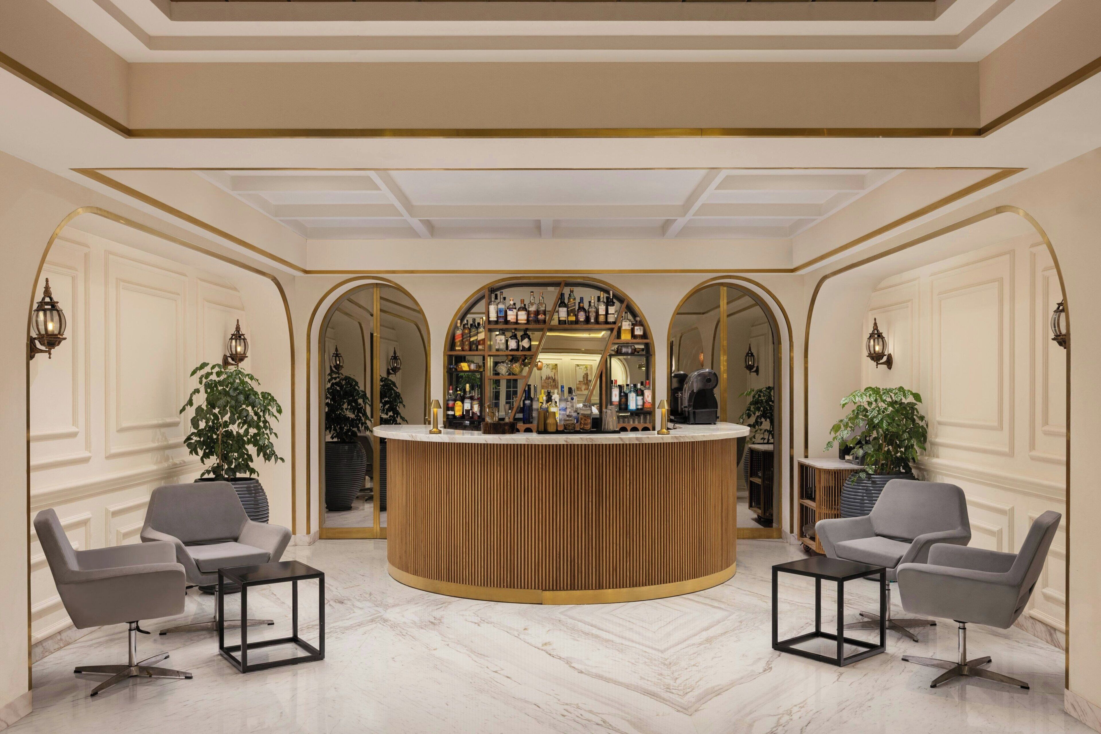 A bar area with a circular counter, two grey armchairs, and a marble floor.