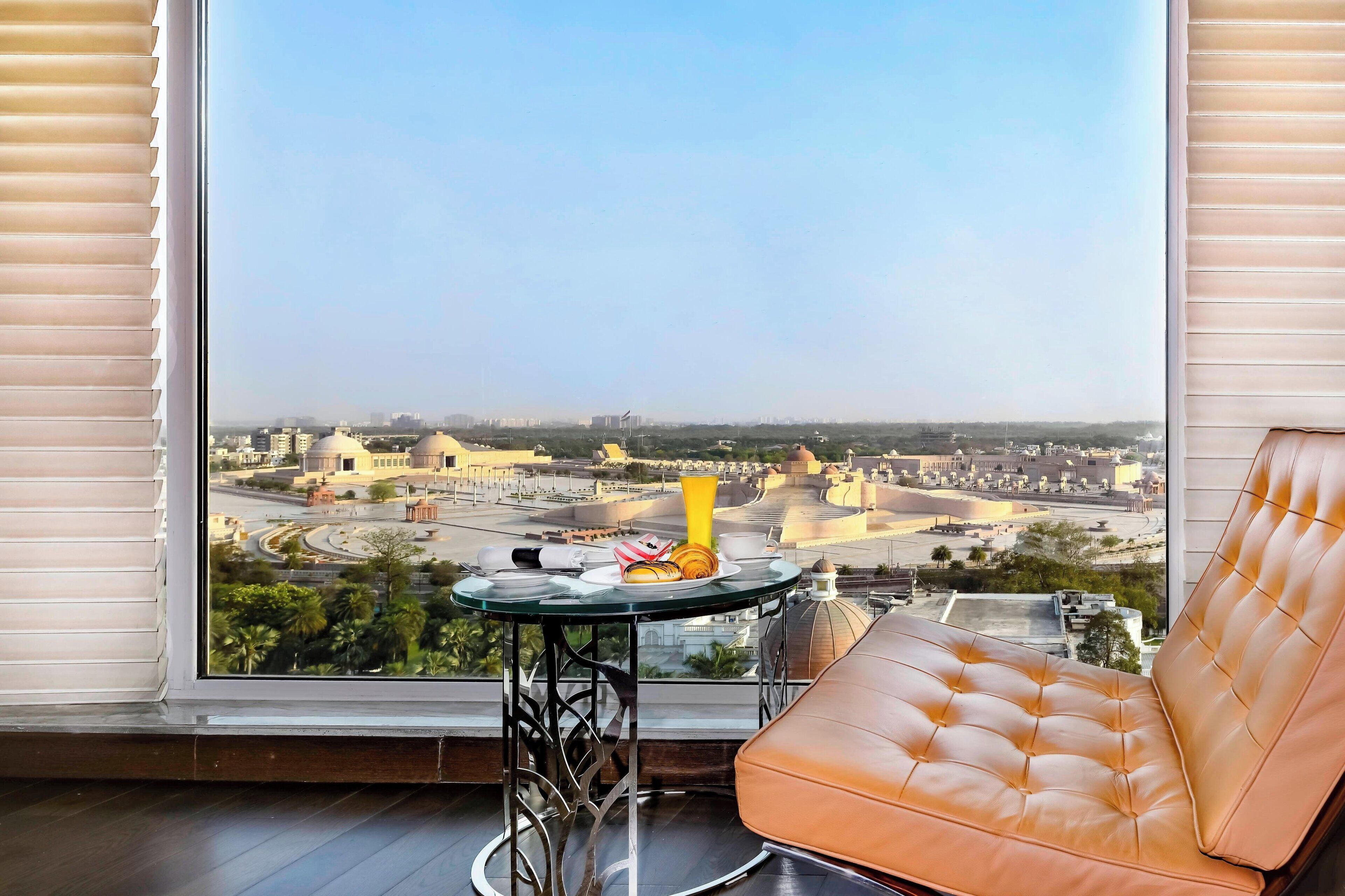 A balcony with a leather chair and a small table with a plate of food and a yellow vase.