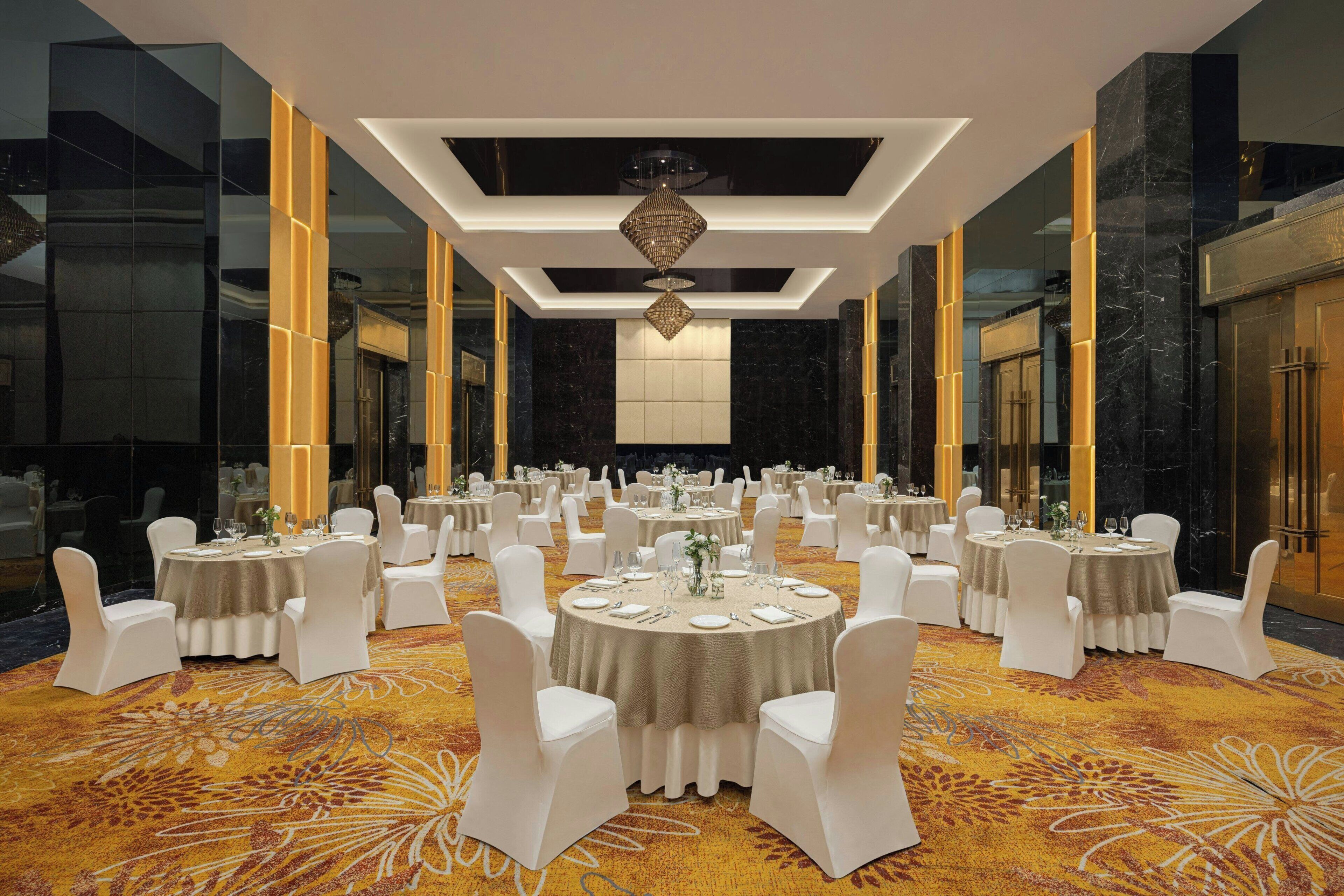 A banquet hall with round tables, white chairs, and a carpeted floor.
