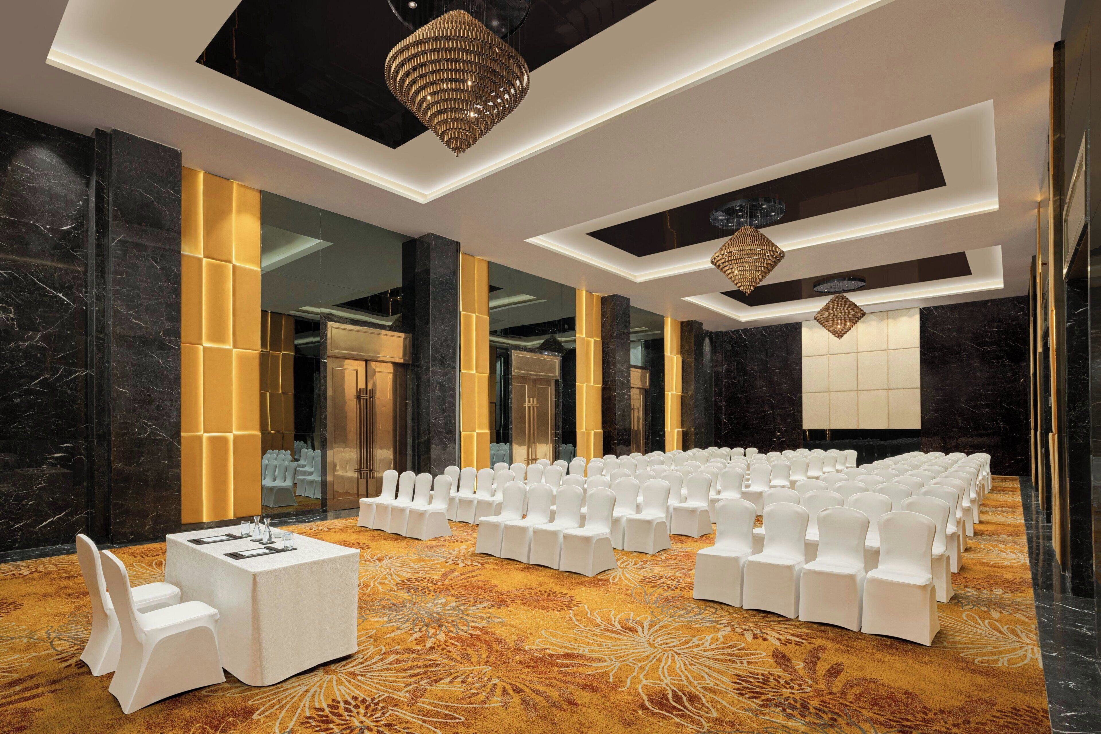 A conference room with rows of white chairs, a table with chairs, and a patterned carpet.