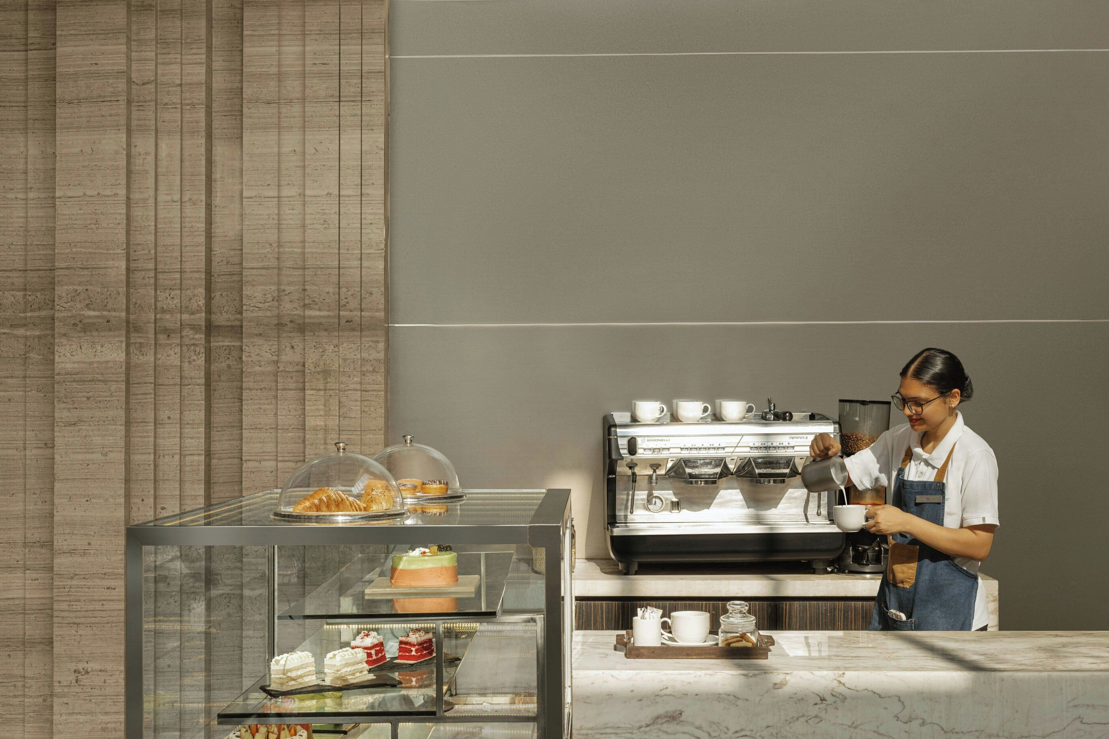 Un café moderne avec une vitrine, une machine à café et un comptoir où se trouvent une cafetière et des tasses.