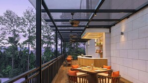 A restaurant with a glass-enclosed balcony, wooden flooring, and orange cushioned chairs. - Renaissance Lucknow Hotel (Lucknow)
