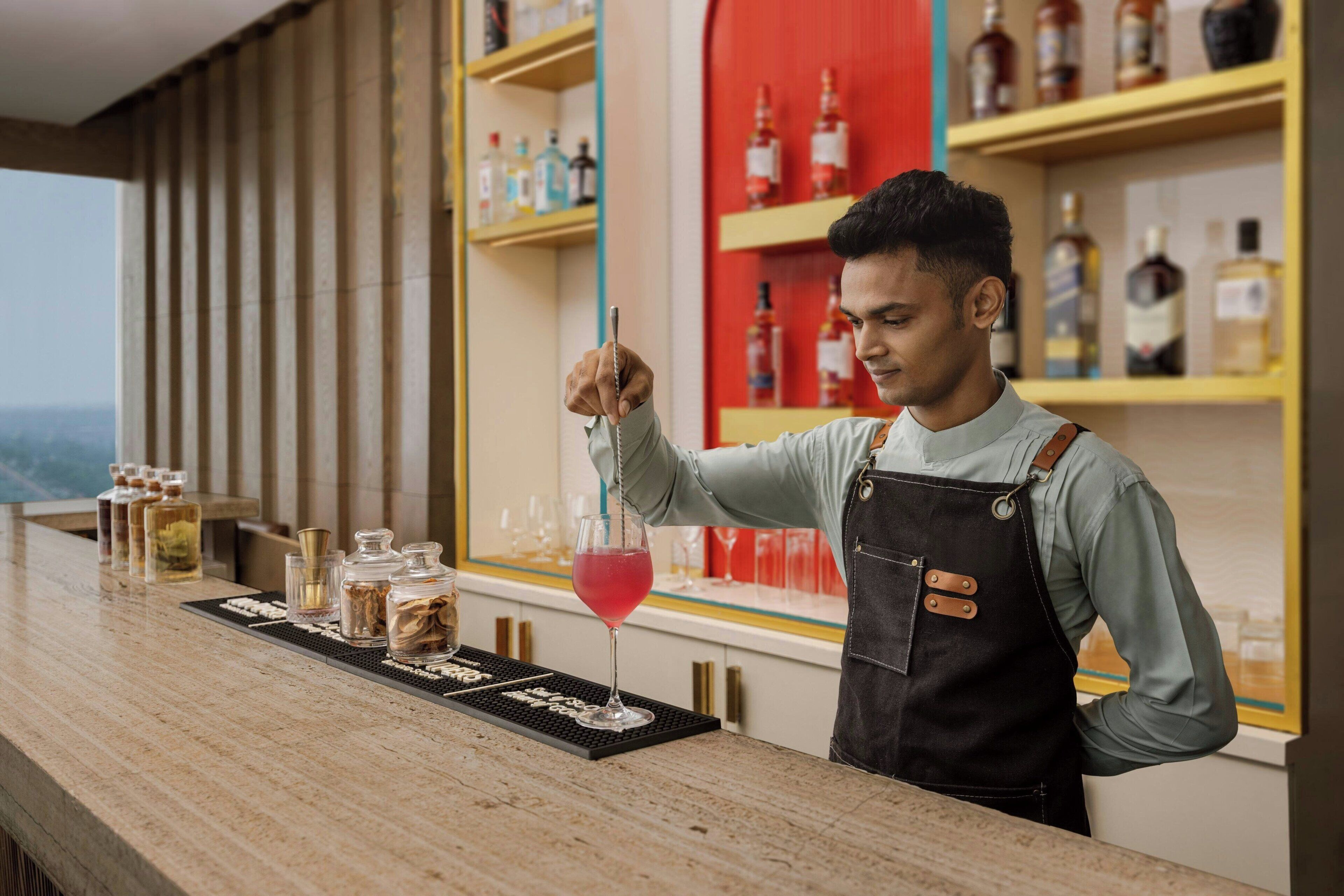 A bar area with a bartender, shelves with bottles, and a bar counter with glasses and bottles.