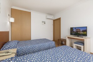 Una habitación de hotel con dos camas, un escritorio con televisor y un armario de madera.