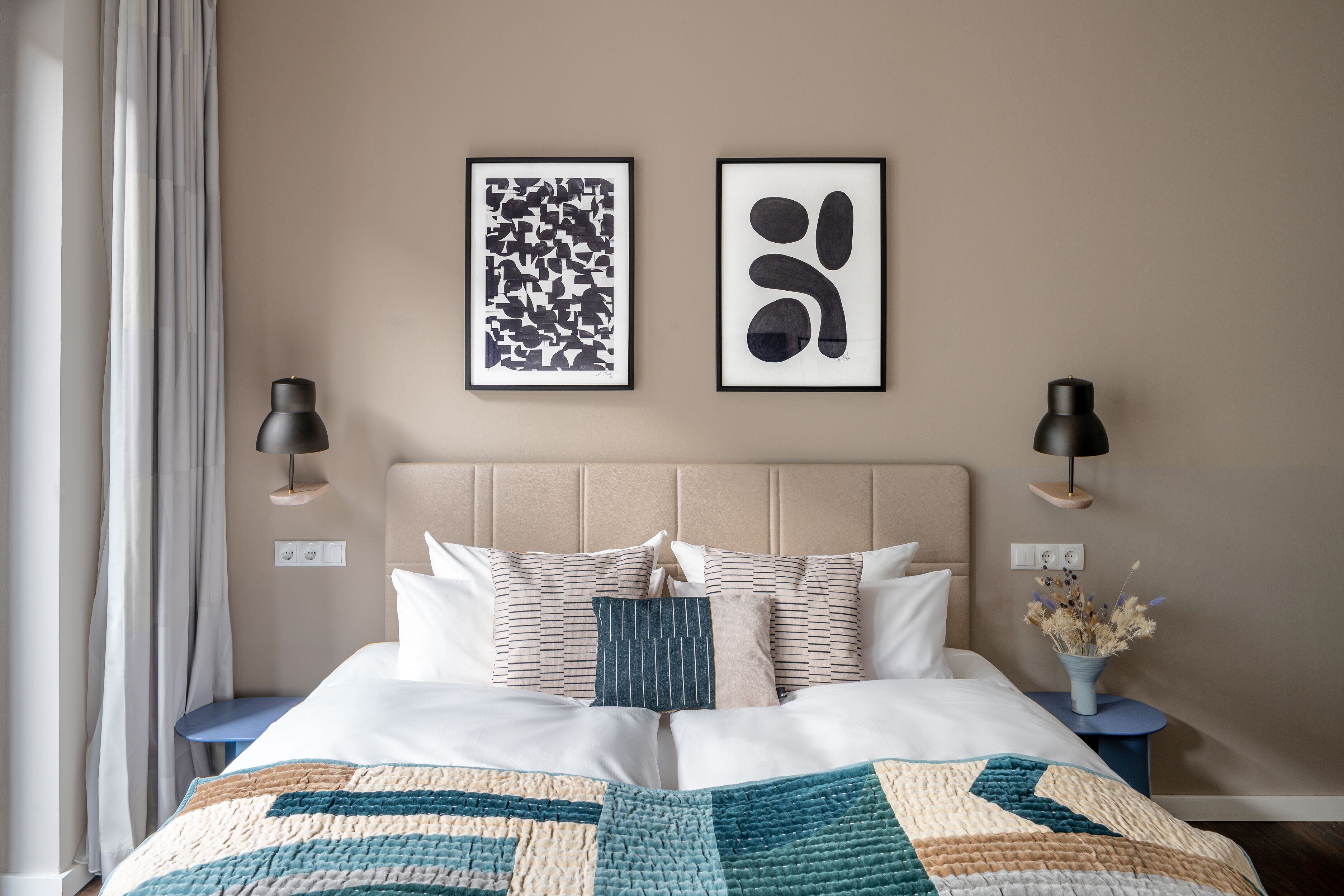 Ein ordentlich bezogenes Bett mit einer Decke, zwei Nachttische mit Lampen und zwei gerahmte Kunstwerke an der Wand.