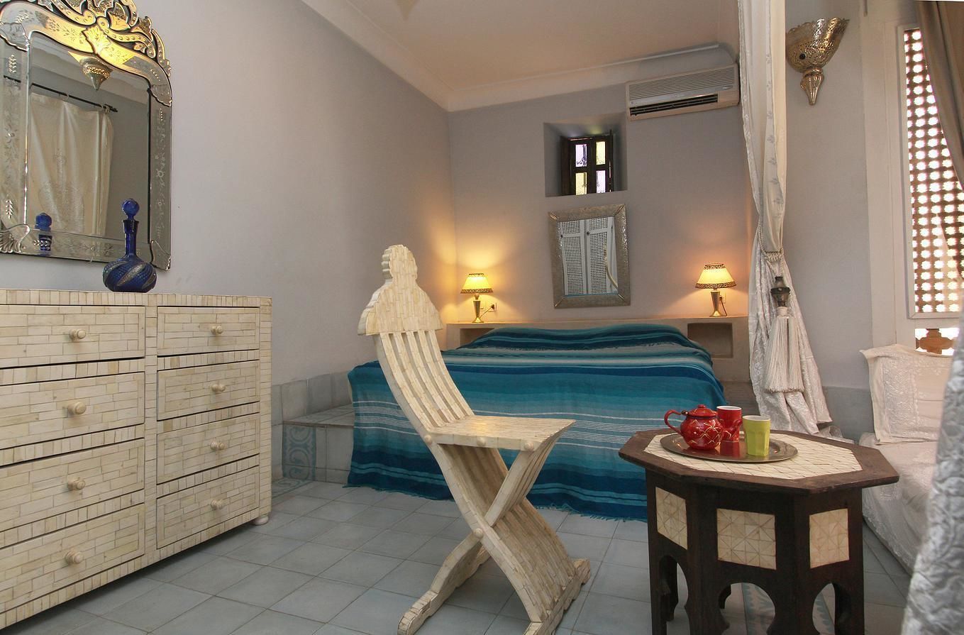 Un dormitorio con una cama, una silla de madera, un aparador, una mesa con una bandeja y un espejo.