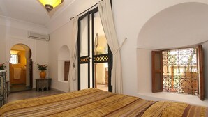 Une chambre dotée d’un grand lit, d’une fenêtre ornée de barreaux en fer forgé et d’une porte à motifs en treillis.