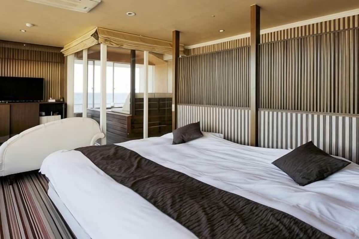 Quarto de hotel com uma cama grande, televisão, área de estar com vista e varanda.
