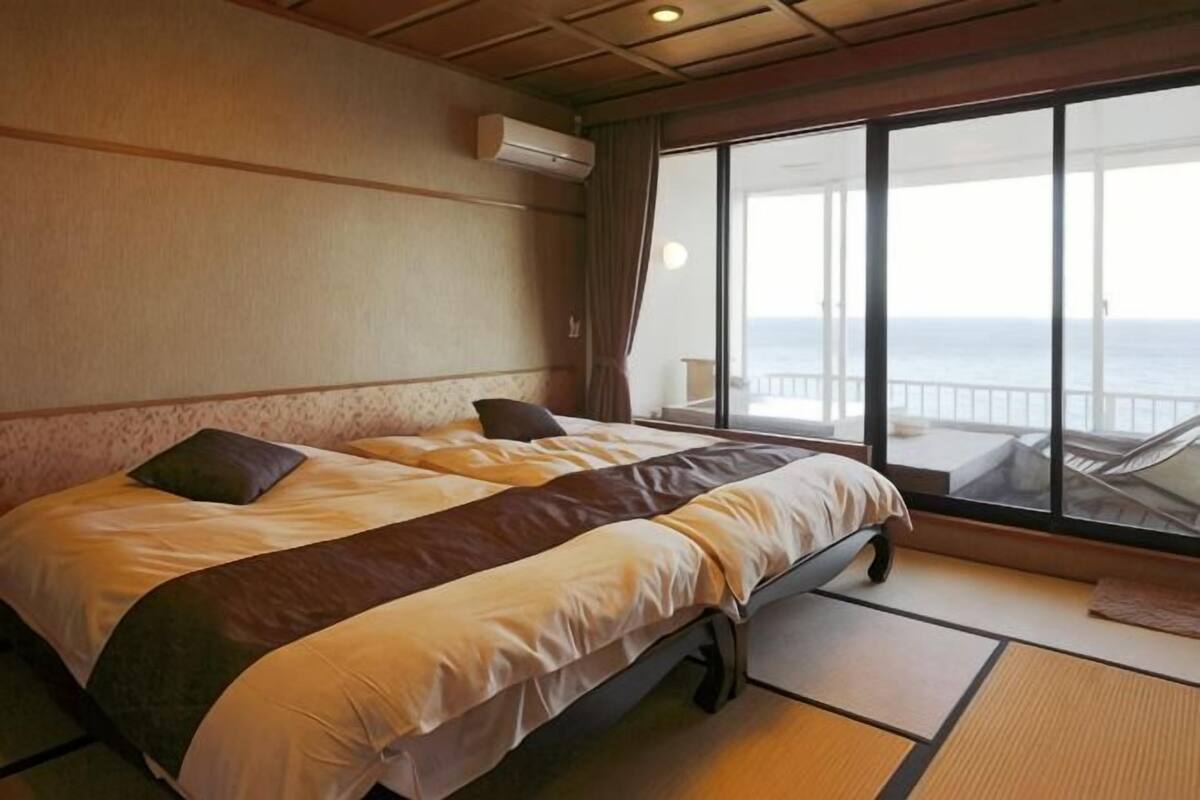Quarto com cama, vista para o mar e varanda com cadeiras.
