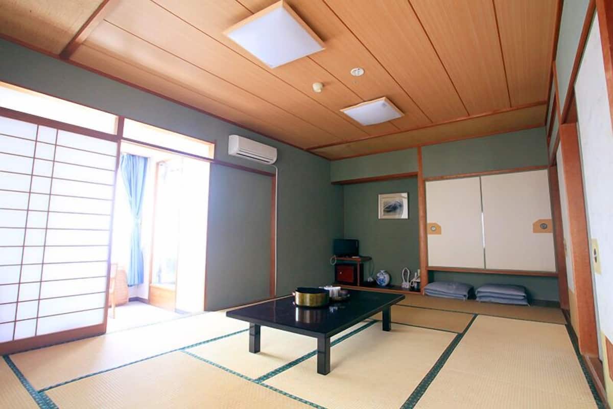 Um quarto japonês tradicional com tatames, uma mesa baixa, portas deslizantes e um ventilador de teto.
