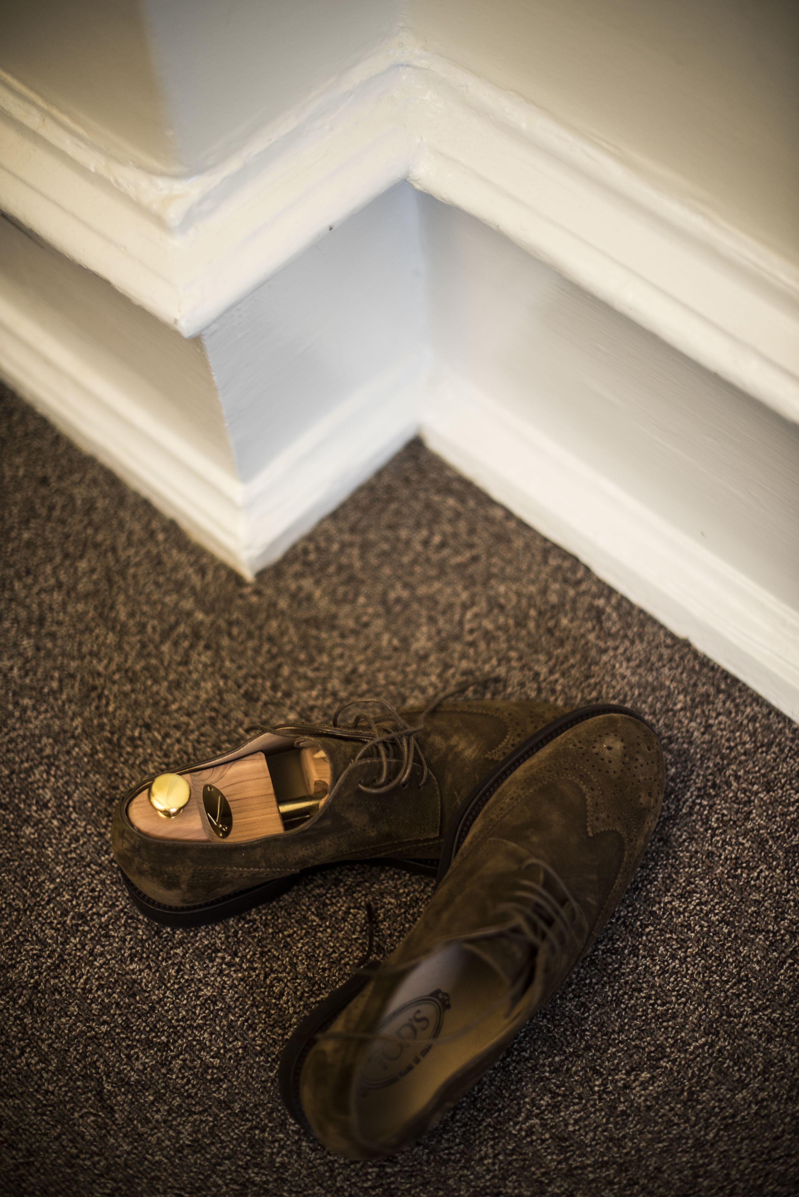 A pair of shoes on a carpeted floor next to a white baseboard.