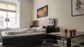 Habitación de hotel con una cama, un escritorio con dos sillas, una lámpara y un cartel en la pared.