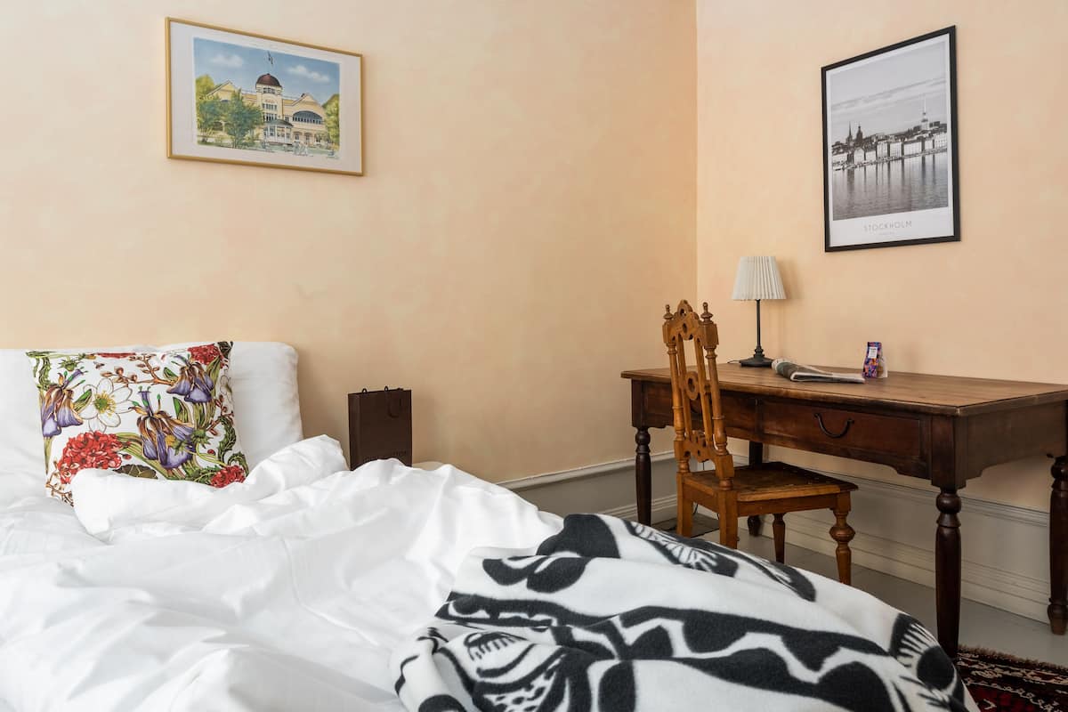 Habitación de hotel con cama, escritorio, silla, lámpara y dos cuadros en la pared.