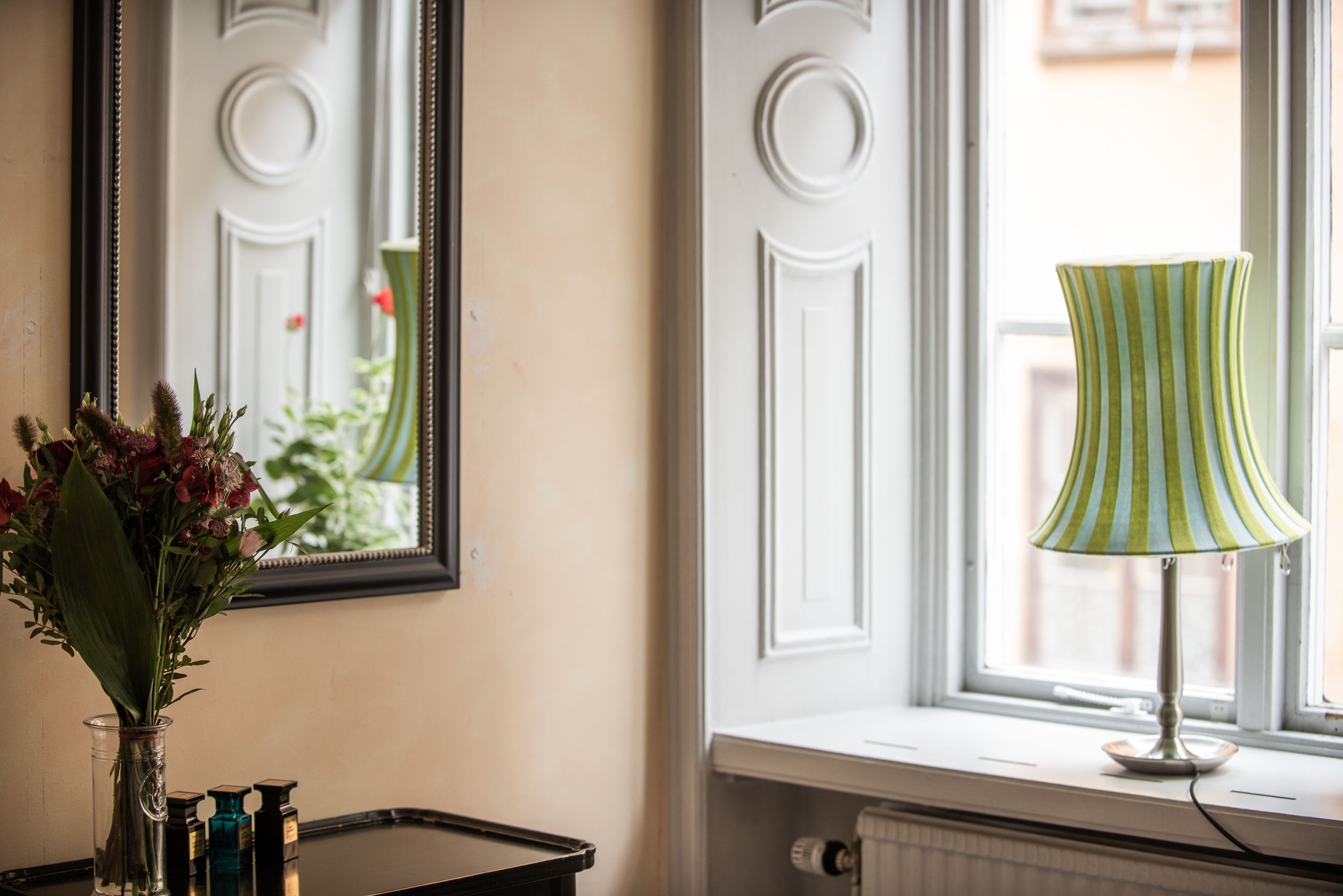 A room with a window, a lamp, and a vase with flowers.