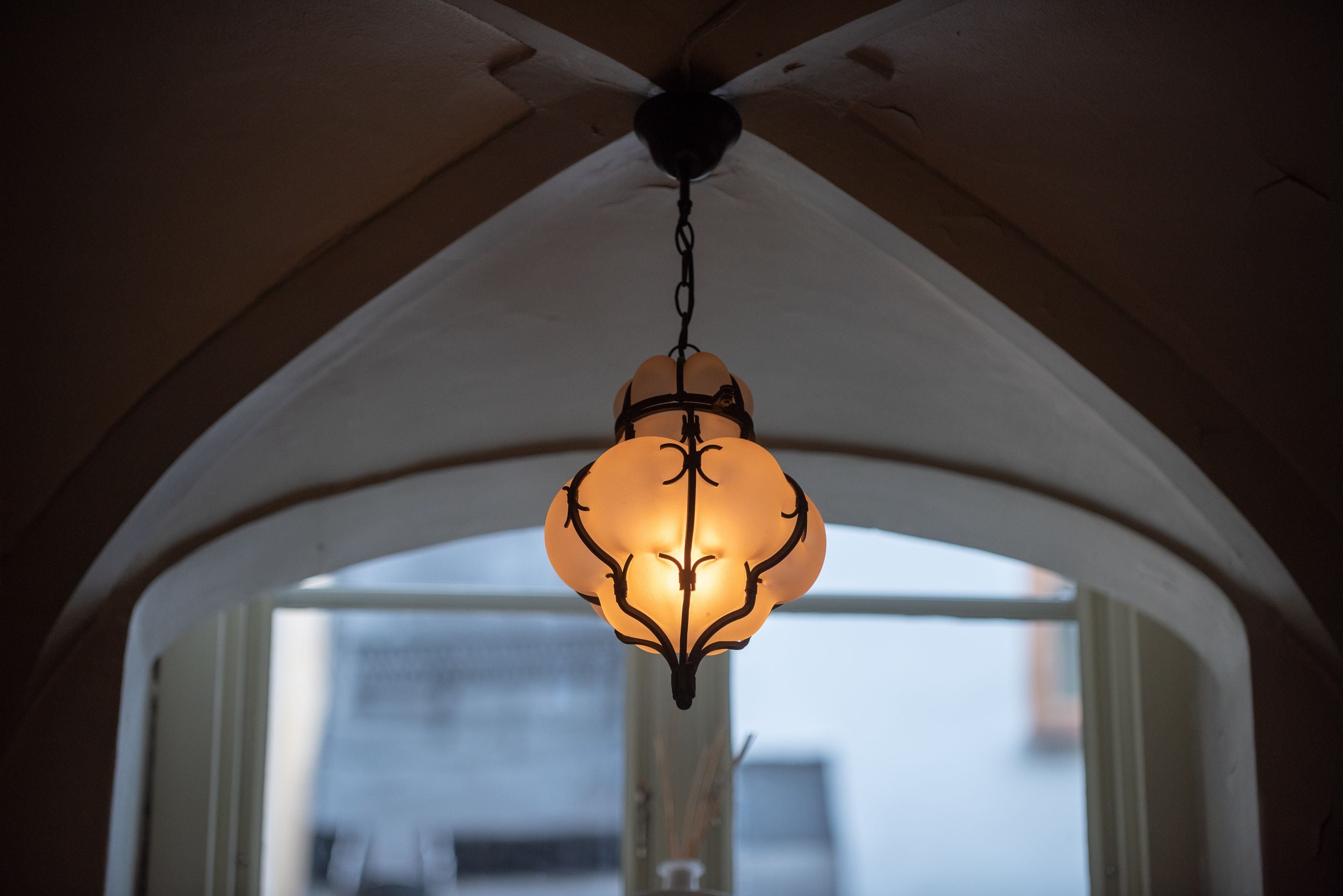 A ceiling fan with a light fixture in a room with an arched doorway and a window.