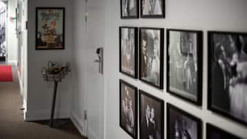 Un pasillo con fotografías blanco y negro enmarcadas en la pared, una pequeña mesa con una cesta y un objeto rojo en el suelo.