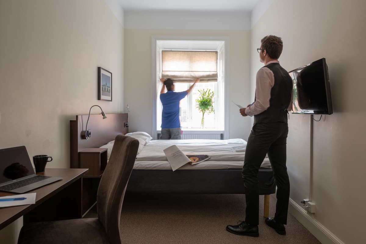Habitación de hotel con cama, escritorio con computadora portátil, silla, televisor montado en la pared y ventana con vistas al exterior.