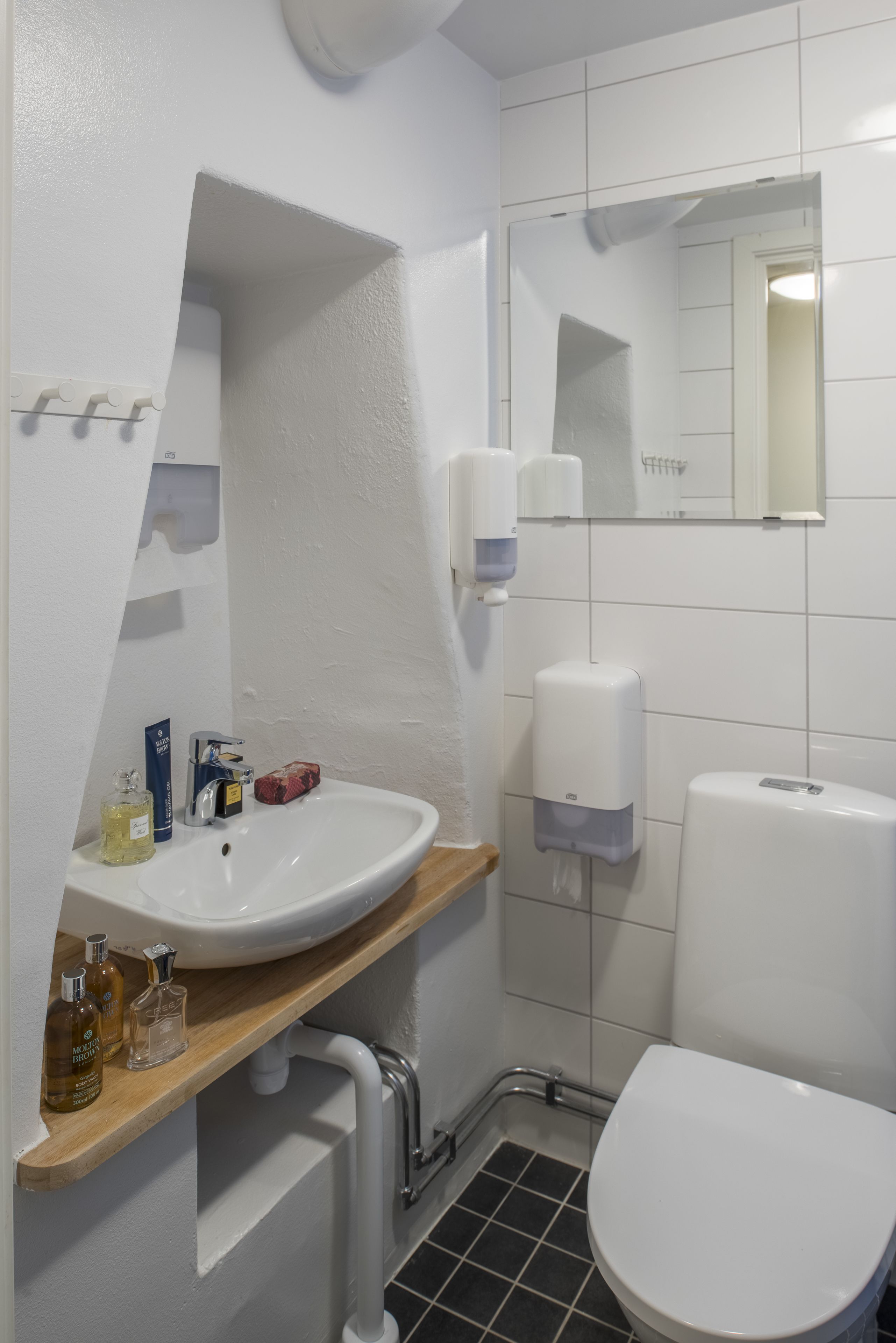 Casa de banho moderna com lavatório branco, espelho, sanita e dispensadores de sabonete.