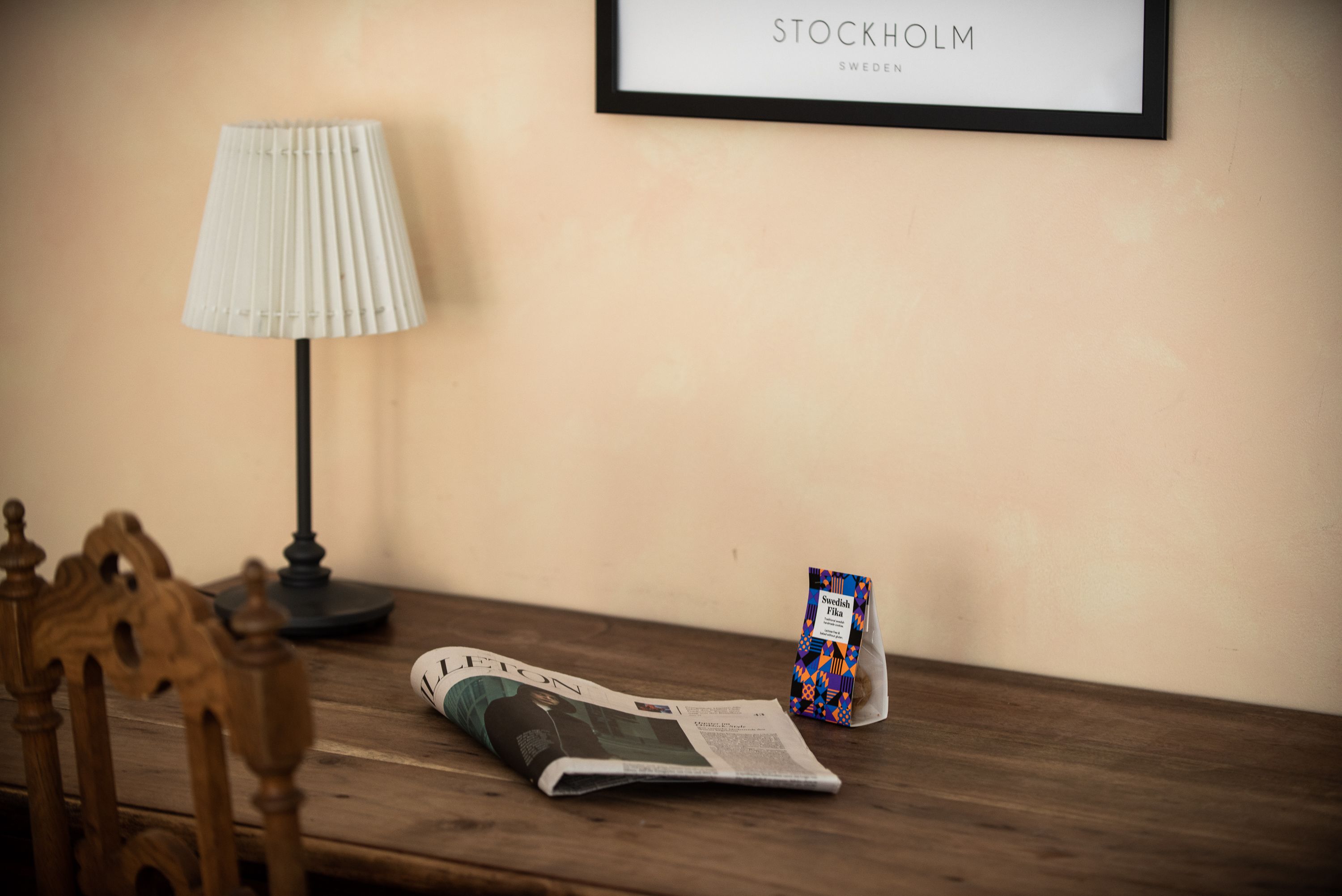 Una mesa de madera con un periódico, una lámpara y un cartel enmarcado que dice 'STOCKHOLM SUECIA'.