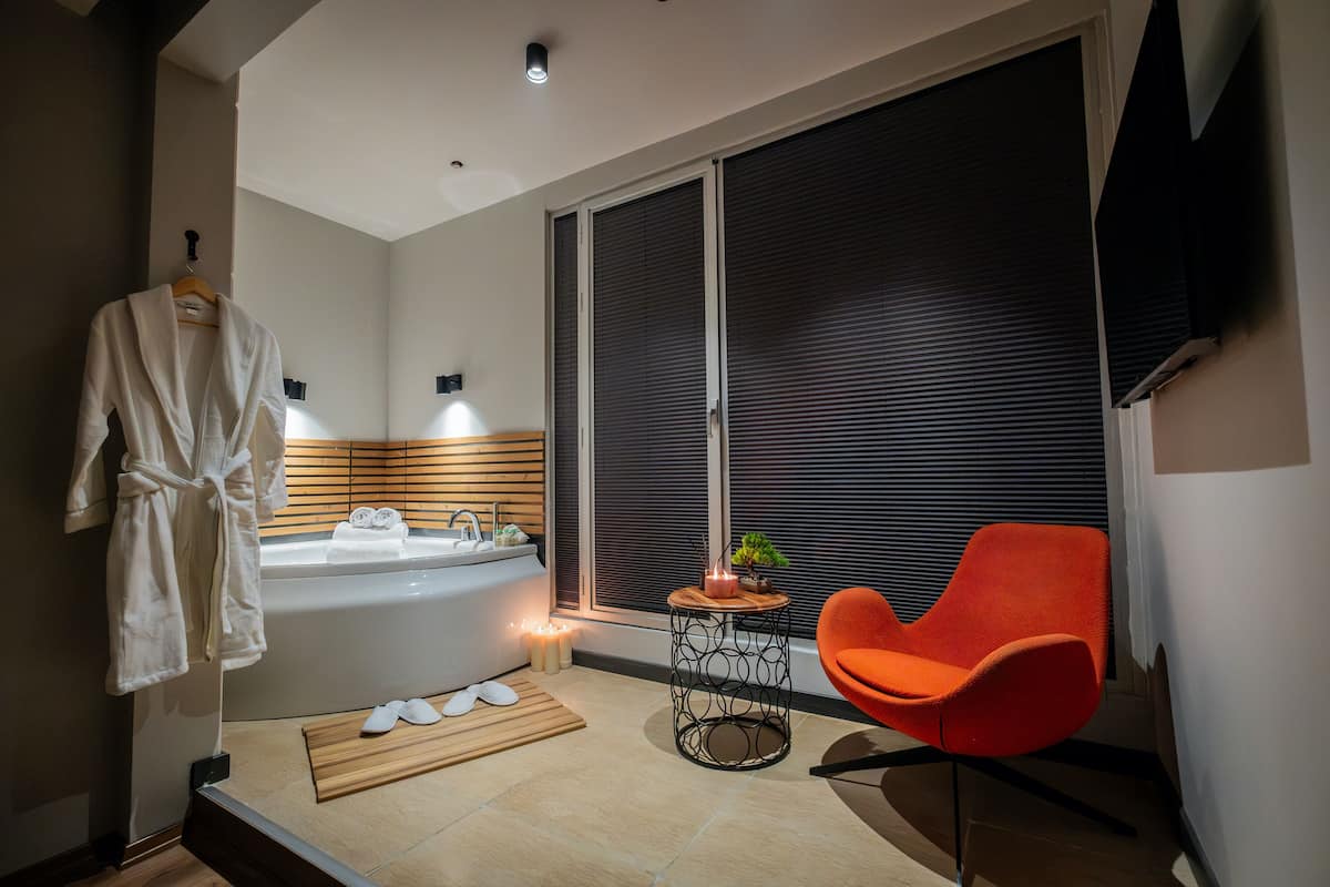 A modern bathroom with a bathtub, a wooden side table with candles, and an orange chair.