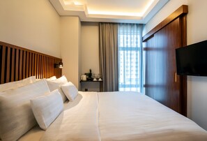 A hotel room with a large bed, a flat-screen TV, a wooden headboard, a bedside table with a lamp, and a window with curtains. - Discovery Hotel (Istanbul)