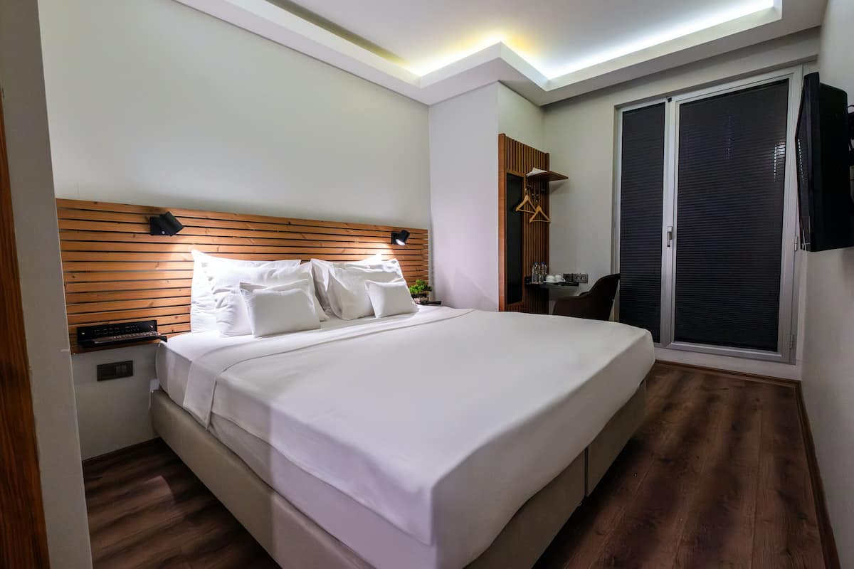 A hotel room with a large bed, a wooden headboard, a bedside table with a lamp, a wardrobe, and a television mounted on the wall.