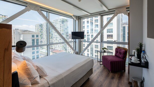 A modern bedroom with a large bed, a chair, a small table, and a TV mounted on the wall. - Discovery Hotel (Istanbul)