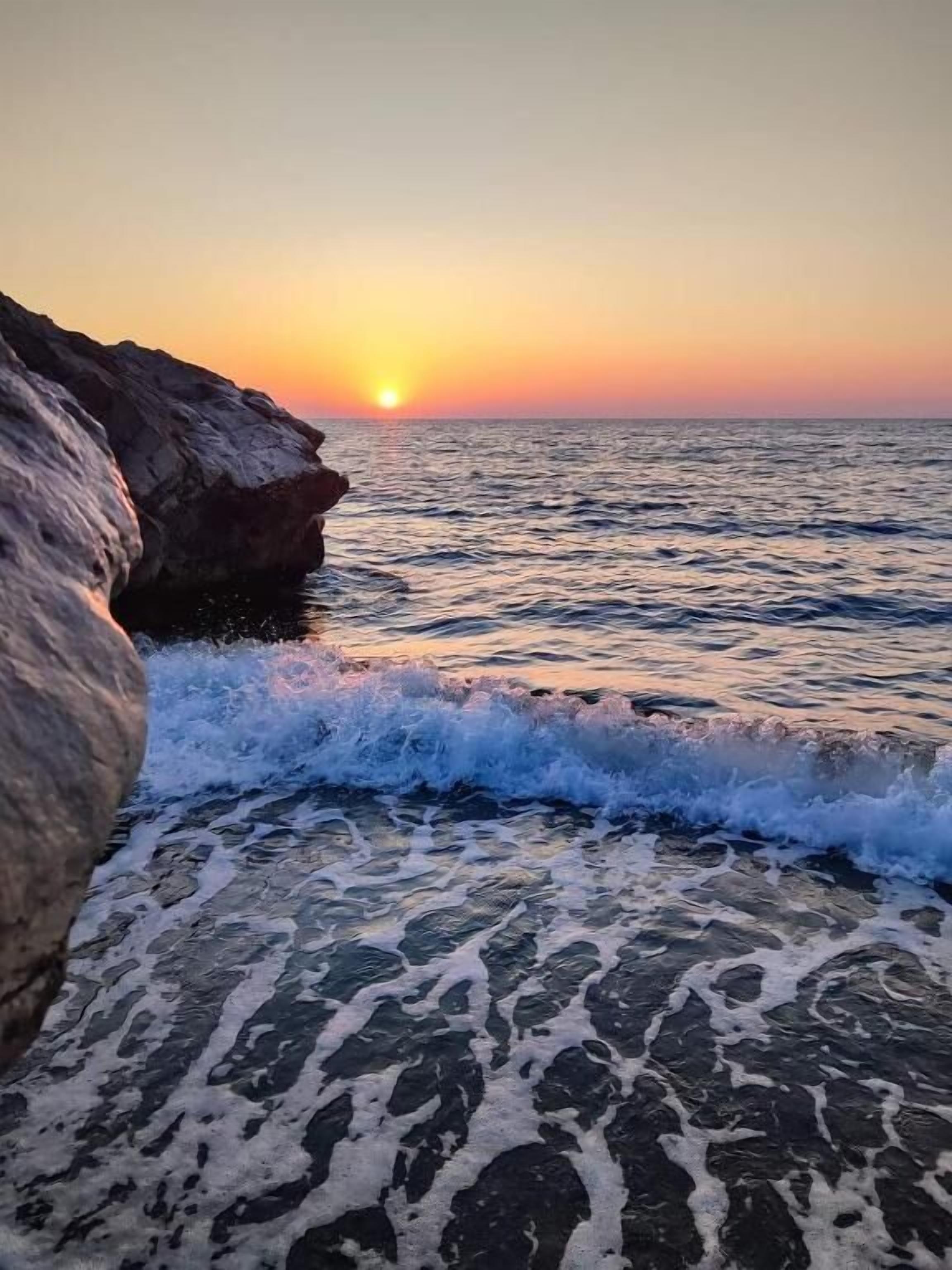 A coastal scene with waves crashing onto a rocky shore during sunset.