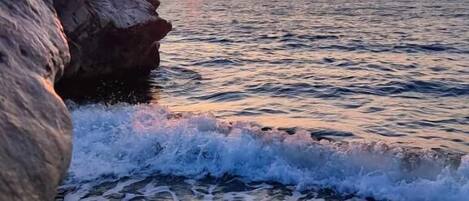 A coastal scene with waves crashing onto a rocky shore during sunset.