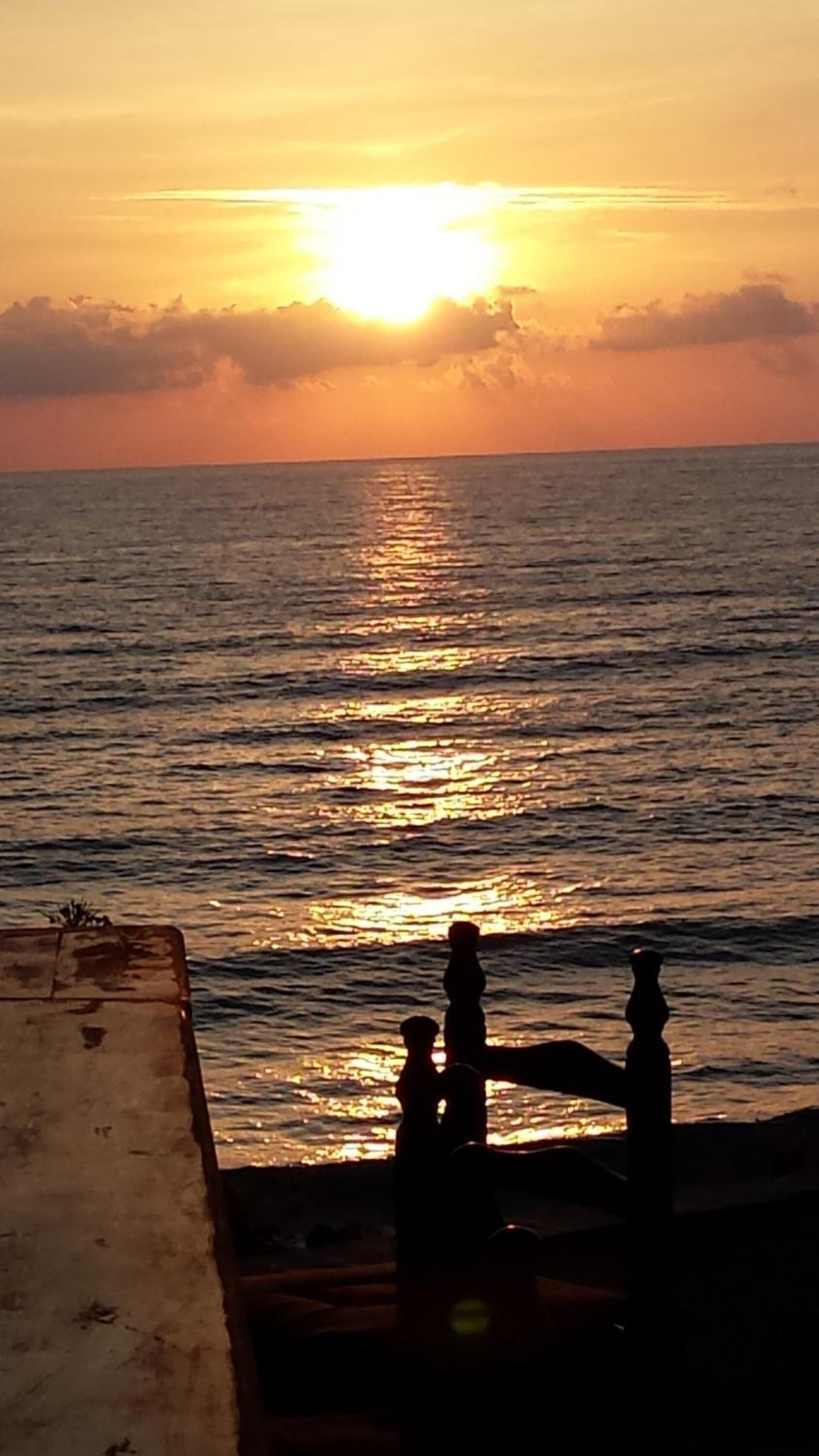 A sunset over a body of water with a silhouette of people and a railing in the foreground.