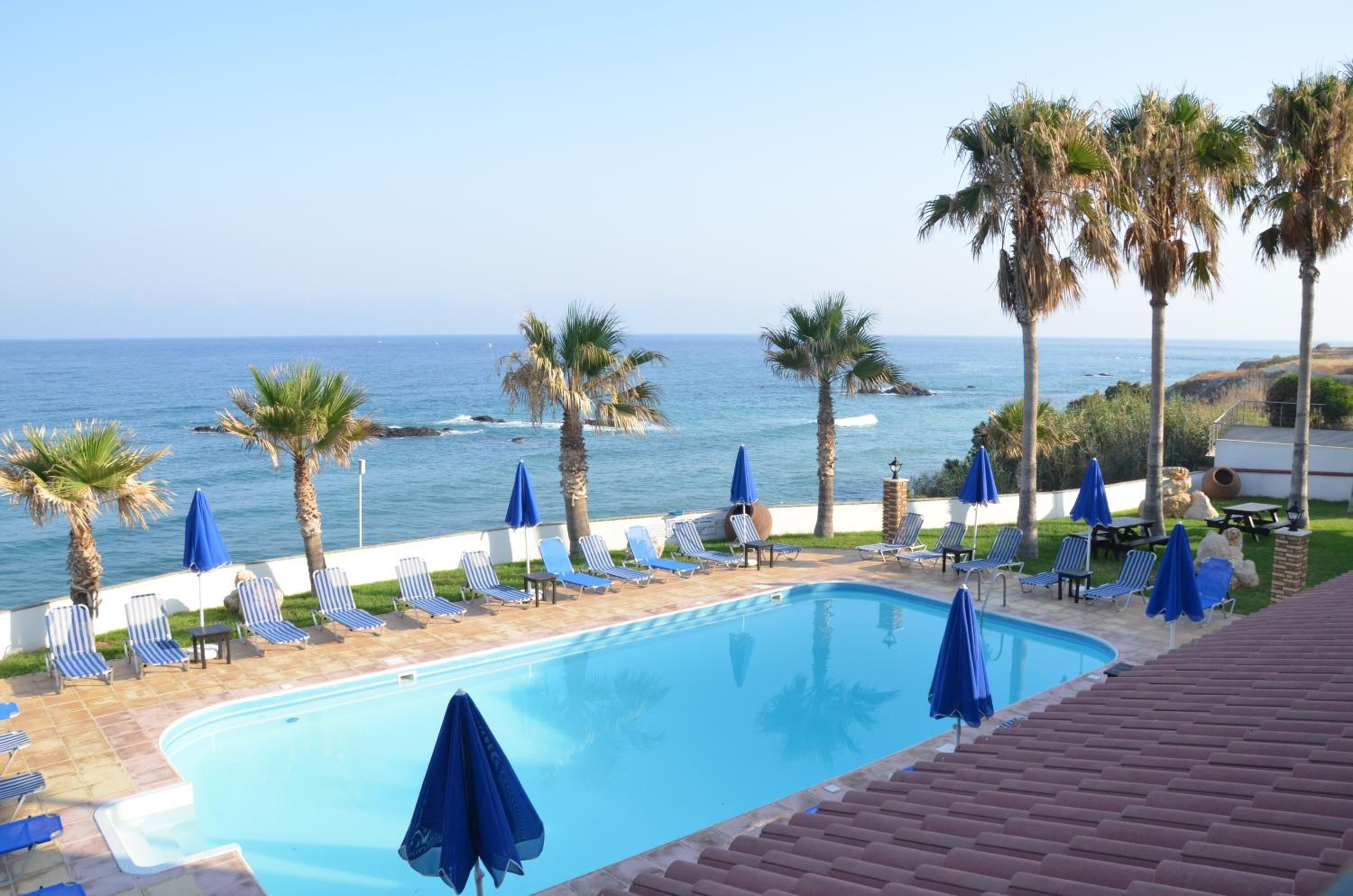 A pool area with lounge chairs and umbrellas, overlooking the ocean.