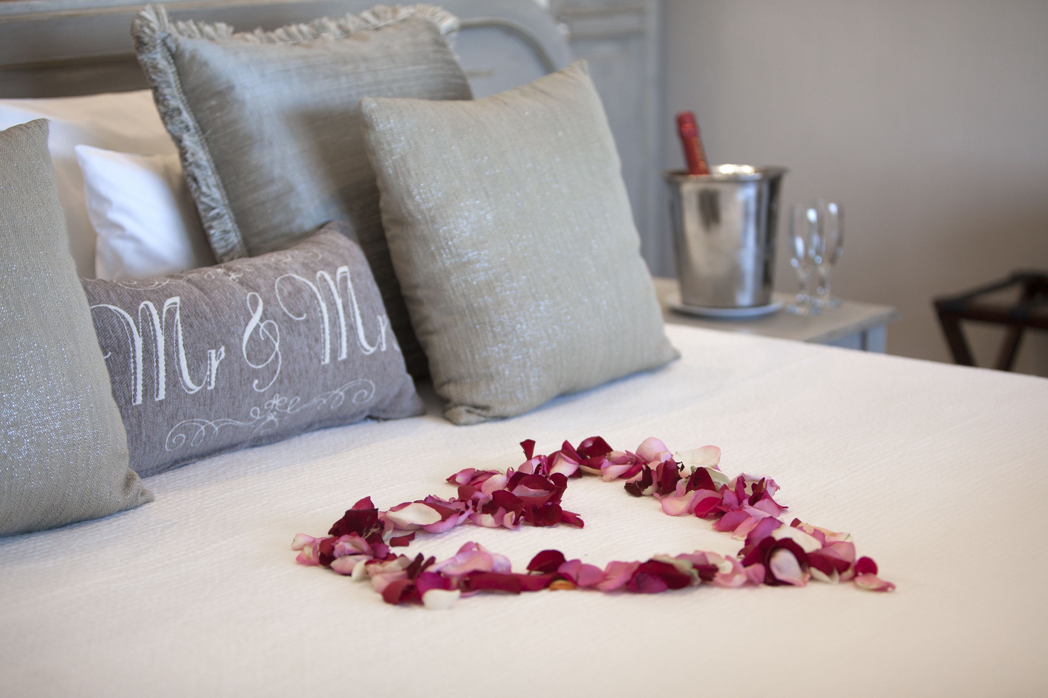 A neatly made bed with decorative pillows and a heart-shaped arrangement of rose petals on the bedspread.
